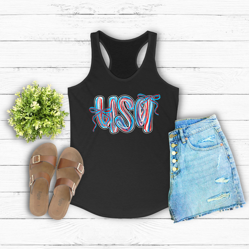 Black tank top with 'USA' print, sandals, and denim shorts on a wooden surface.