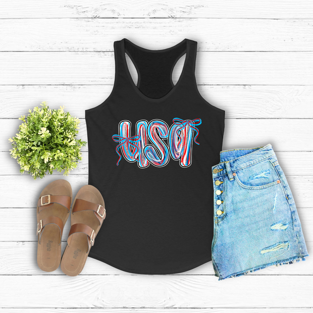 Black tank top with 'USA' print, sandals, and denim shorts on a wooden surface.